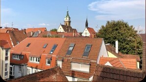 A residential area with red-tiled roofs, a church with a spire, and a tree in the foreground. - FeWo BC 40 (Stuttgart)