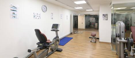 A gym with exercise equipment, a clock, and instructional posters on the wall.