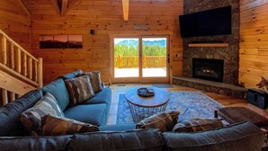 L’intérieur chaleureux d’un chalet en bois, avec une cheminée en pierre, un grand canapé et un balcon offrant une vue imprenable sur les montagnes.