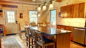 L’intérieur d’une cabane en bois comprend une grande table à manger, des chaises, un coin cuisine et un réfrigérateur encastré.