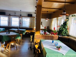 A restaurant with wooden tables and chairs, green tablecloths, and large windows with curtains. - Garni Appartement Collina (Samnaun)