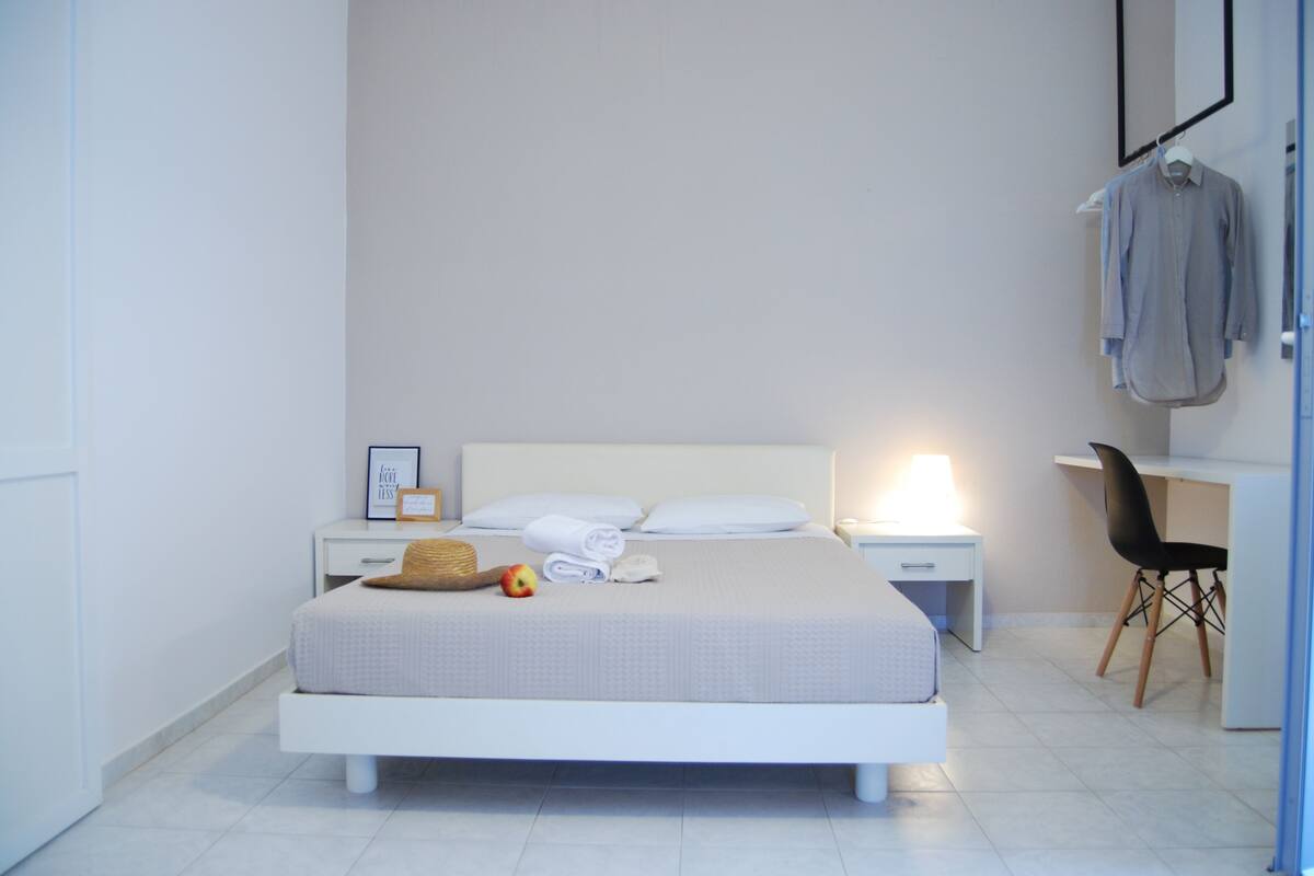 Een moderne hotelkamer met een opgemaakt bed, een nachtkastje met lamp, een stoel en een bureau.