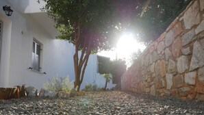 A courtyard with a stone wall, a tree, and a building with a window. - Galini Rooms & Apartments Syros (Syros)