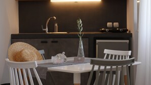 A modern kitchen with a dark countertop, a sink, and a shelf above. There is a vase with a plant on the counter. - Galini Rooms & Apartments Syros (Syros)