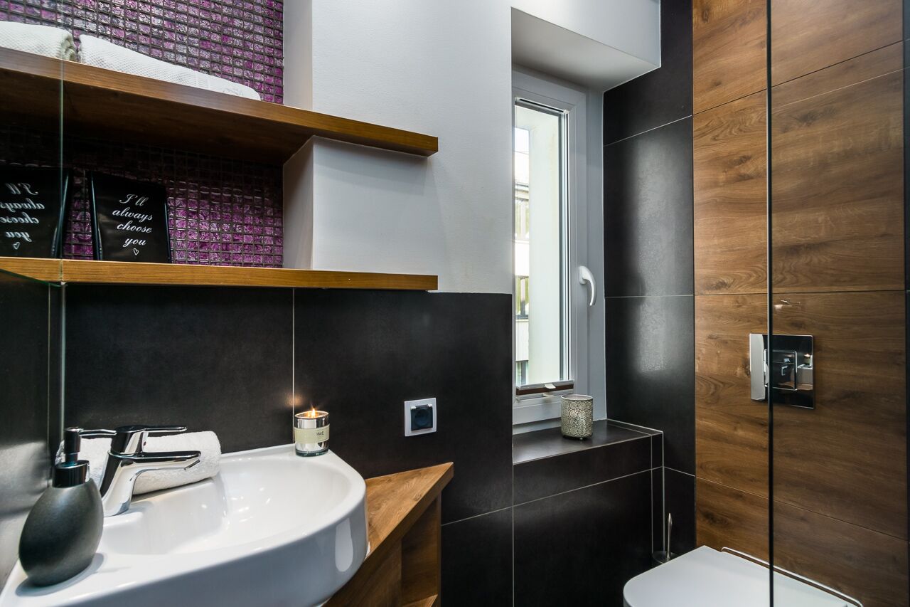 Un baño moderno con un lavabo blanco, paneles de madera oscura y un estante con objetos decorativos.