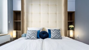 A neatly made bed with a tufted headboard, bedside tables with lamps, and built-in shelving. - Elite Apartments Sopot Zacisze (Gdansk)