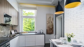 A modern kitchen with white cabinetry, a built-in microwave, and a window overlooking greenery. - Elite Apartments Sopot Zacisze (Gdansk)