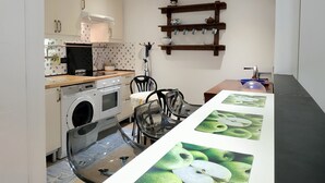 Une cuisine compacte équipée d’un lave-linge, d’un four à micro-ondes et d’un évier. Une étagère en bois, agrémentée d’objets décoratifs, se trouve au-dessus de l’évier.