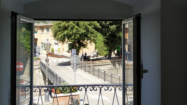 Un balcon doté d’une balustrade en fer forgé, donnant sur une rue bordée d’immeubles et d’arbres.
