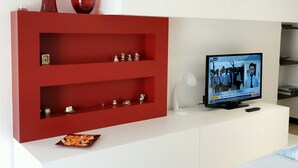 Un salon moderne avec un meuble de rangement rouge pour l’équipement audiovisuel, un téléviseur à écran plat et une console blanche.