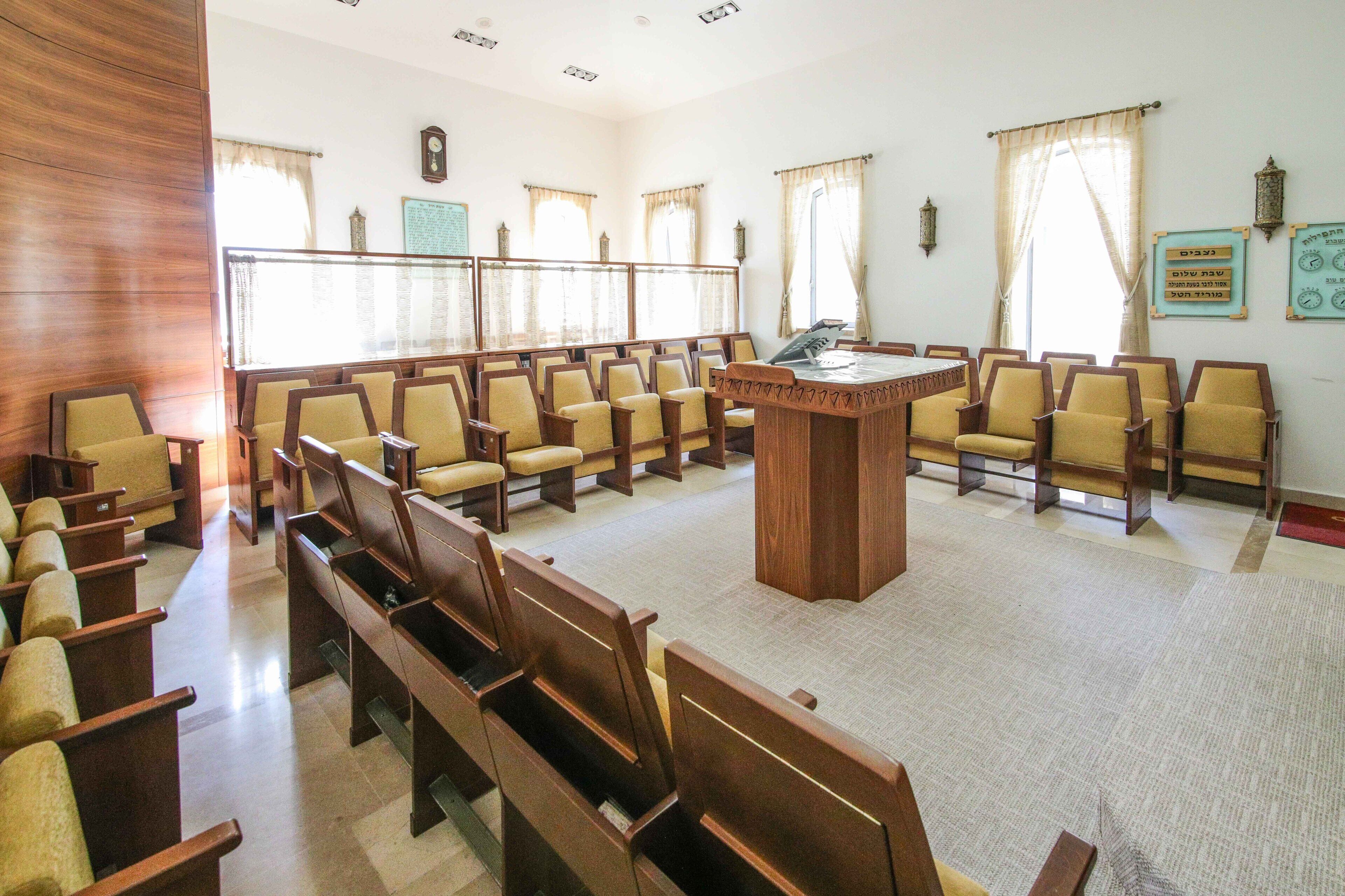A conference room with a large table and multiple chairs, a clock on the wall, and a bulletin board.