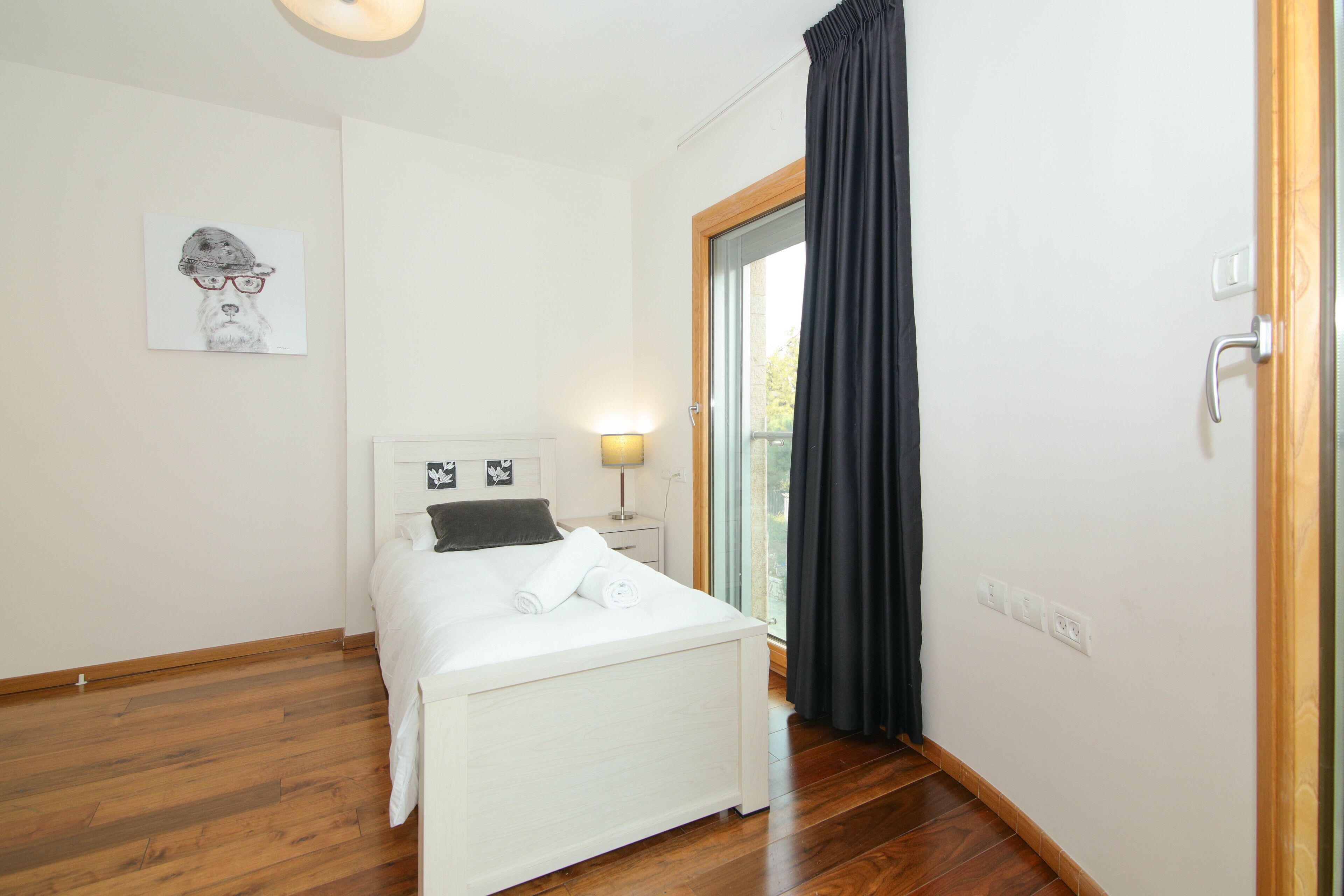 A bedroom with a bed, a nightstand, a lamp, and a window with curtains.
