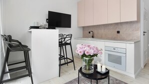A modern kitchen with white cabinets, a black TV, and a small dining area with stools and a vase of flowers.