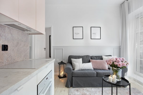 Une cuisine moderne avec un plan de travail en marbre, un canapé gris agrémenté de coussins décoratifs, une petite table d’appoint noire avec des bougies et un vase rempli de fleurs roses.
