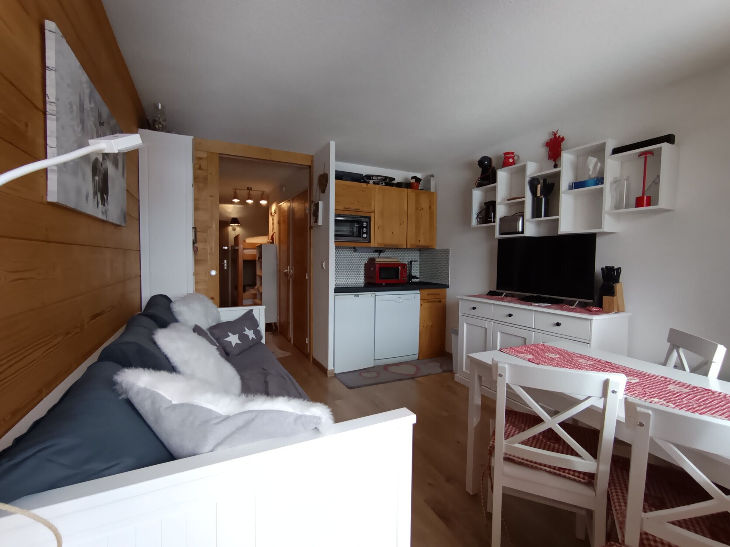 A compact living space with a kitchenette, a sofa with pillows, a dining table with chairs, and a TV.