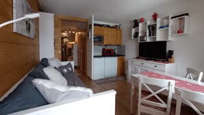 Un espacio habitable compacto con kitchenette, un sofá con almohadas, una mesa de comedor con sillas y un televisor.