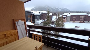 Un balcón con mesa y sillas de madera, con vistas a una montaña nevada y edificios.