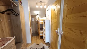 Un pasillo estrecho con paredes de madera, un perchero, un refrigerador blanco y una alfombra estampada.