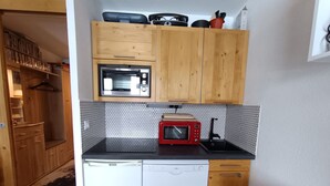 Cocina compacta con armarios de madera, microondas, tostadora roja y lavavajillas.
