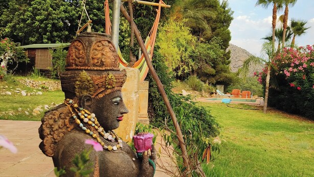 A statue of a deity holding a flower, a hammock, and a small table with chairs in a garden setting. - Casa del Paso (Bolulla)