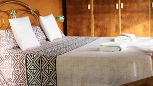 A neatly made bed with patterned bedding, a wooden headboard, and a wooden wardrobe in the background. - Casa del Paso (Bolulla)