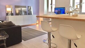 A modern kitchen with a bar area, white bar stools, and a television displaying a news channel. - Happy Holiday Sanremo (Sanremo)