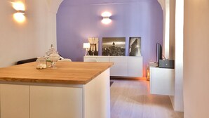 A modern kitchen with a wooden island, white cabinetry, and a purple accent wall. - Happy Holiday Sanremo (Sanremo)