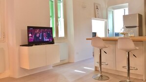 A modern kitchen with a built-in TV, two bar stools, and a refrigerator. - Happy Holiday Sanremo (Sanremo)