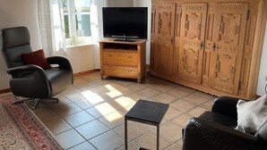 Een woonkamer met een tv op een houten kast, een zwarte leren bank, een klein tafeltje en een kamerkleed met een patroon.