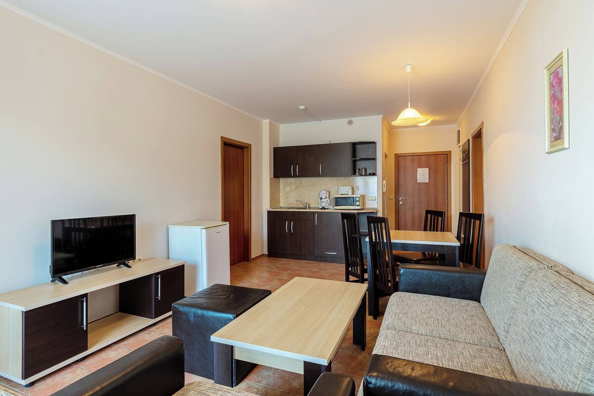 A compact living space with a sofa, a TV, a dining table, and a kitchenette.