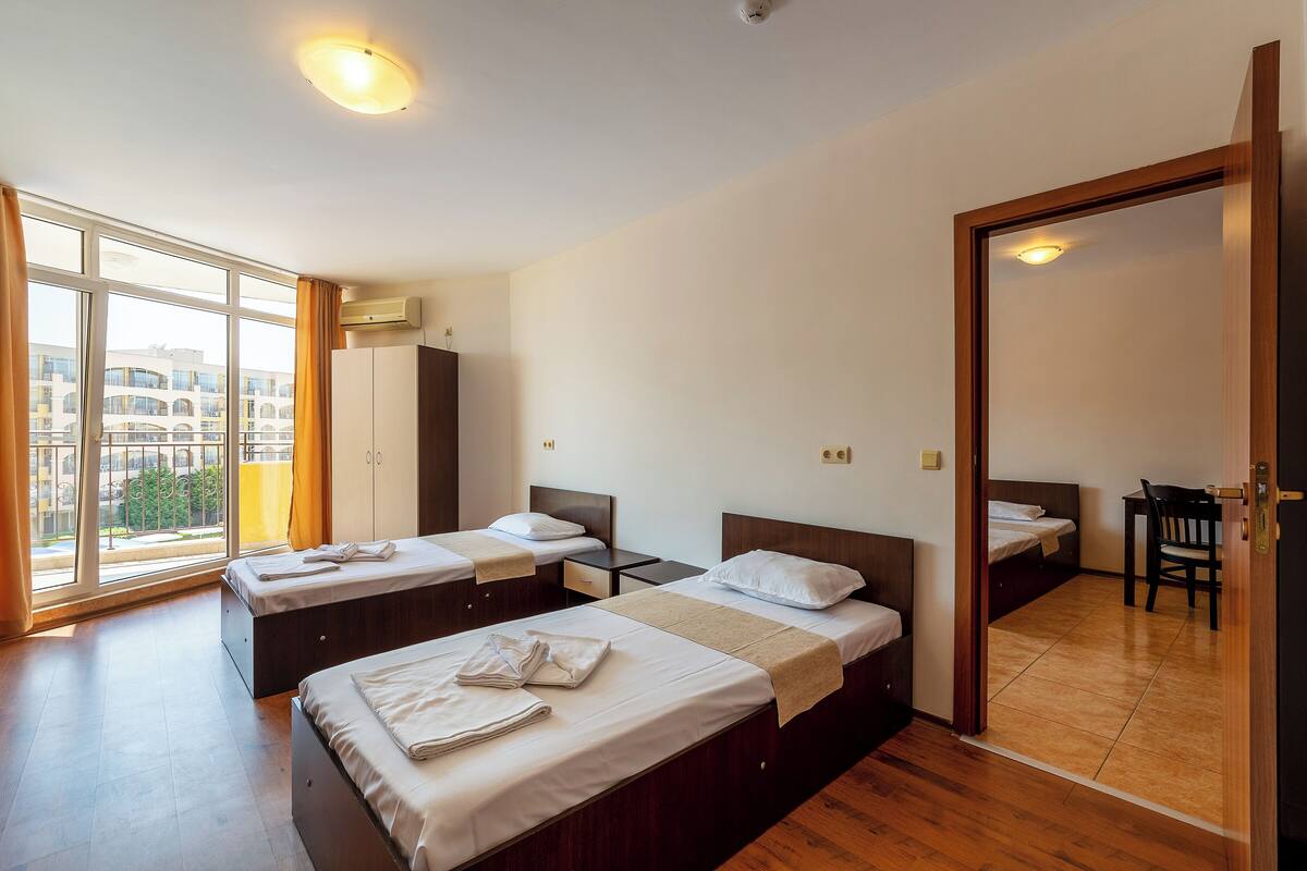 A hotel room with three beds, a desk, and a view of the city.