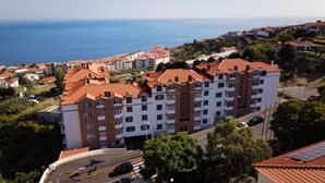 Un hotel a più piani con un tetto in tegole rosse, situato in una zona costiera con vista sul mare.