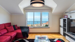 Un soggiorno con un divano rosso, una lampada a sospensione a righe bianche e nere, un'ampia finestra con vista sugli edifici e un mobile TV.