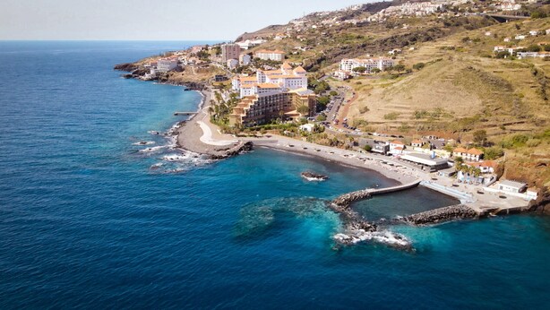 Una cittadina costiera con un porto turistico, edifici dai tetti rossi e una vista limpida sul mare.