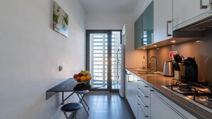 Cozinha moderna com área de refeições, vista através de uma porta de vidro e uma fruteira sobre a mesa.