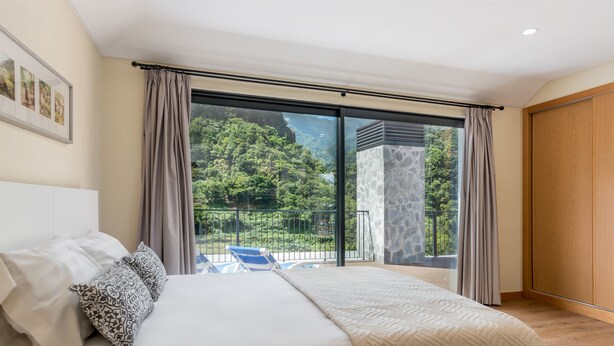 Ein Schlafzimmer mit einem großen Bett, Blick auf einen Balkon mit einer Steinmauer und einer Holztür.