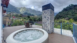 Ein Whirlpool auf einem Balkon mit Blick auf die Berge, einer Steinsäule und einem Tisch mit Stühlen.