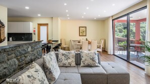 A modern living room with a grey sofa, a kitchen area, and a dining space. - Villa Teresa/1 by Atlantic Holiday (São Vicente)