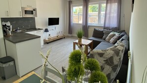 Un apartamento funcional con kitchenette, sala de estar con sofá y televisor, y comedor con mesa y sillas.