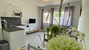 Una cocina moderna con microondas, una mesa de comedor con posavasos y vistas al área de estar con televisor y plantas.