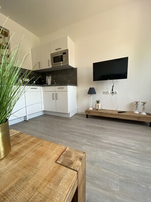 A modern kitchen with white cabinets, a microwave, and a flat-screen TV mounted on the wall.