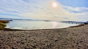 Una playa con un muelle que se adentra en aguas tranquilas bajo un cielo parcialmente nublado.