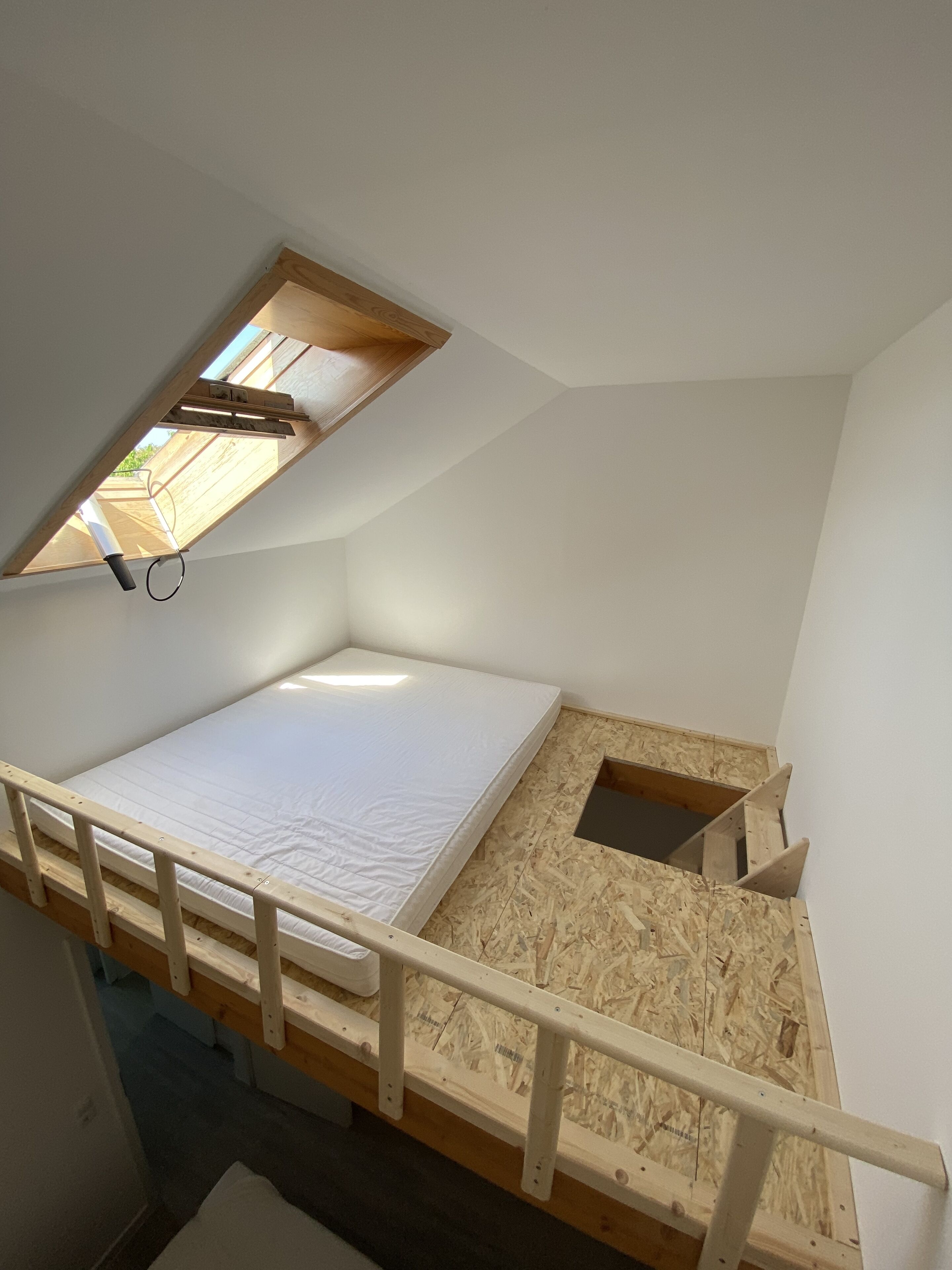 A small, sloped room with a single bed, a skylight, and a wooden floor.