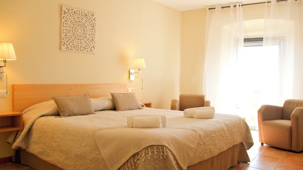 A hotel room with a large bed, two bedside tables, a chair, and a window with curtains. - Santuari de Terrades (Terrades)