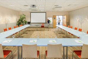 Een vergaderzaal met een lange tafel, stoelen, een projectiescherm en een plant.