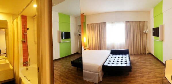 A hotel room with a bed, a television, a desk, and a bathroom.