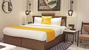 A hotel room with a large bed, a desk, a chair, a painting on the wall, and a mirror. - Bloom Boutique Gk-1 (New Delhi)