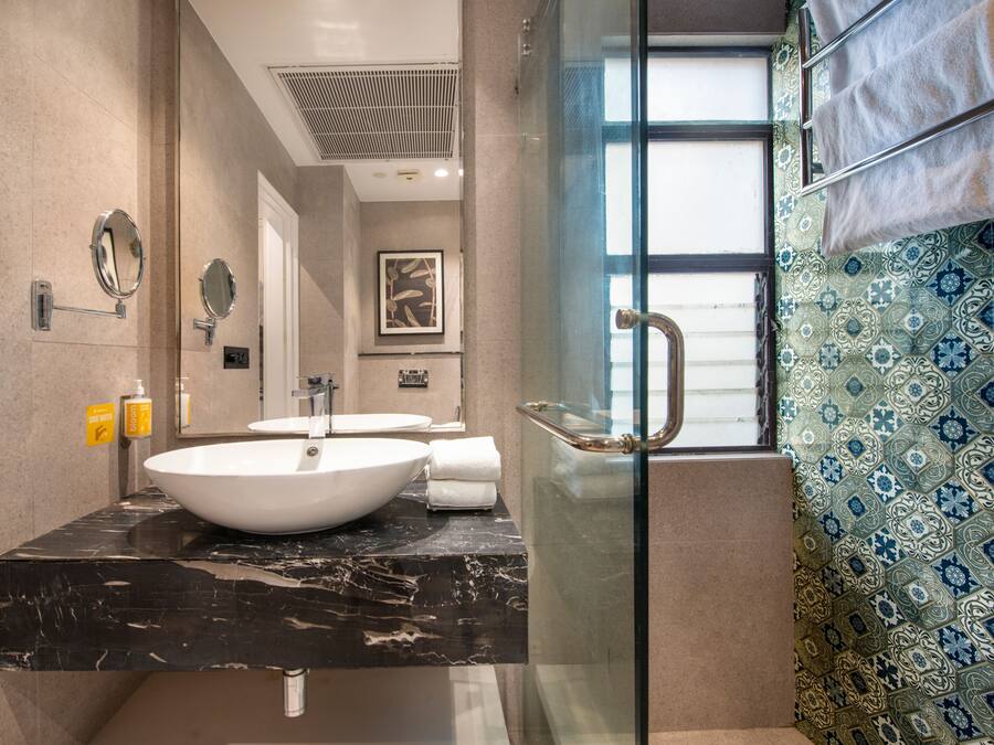 Un baño moderno con un lavamanos grande de color blanco, cabina de ducha con paredes de vidrio y baldosas con diseño.