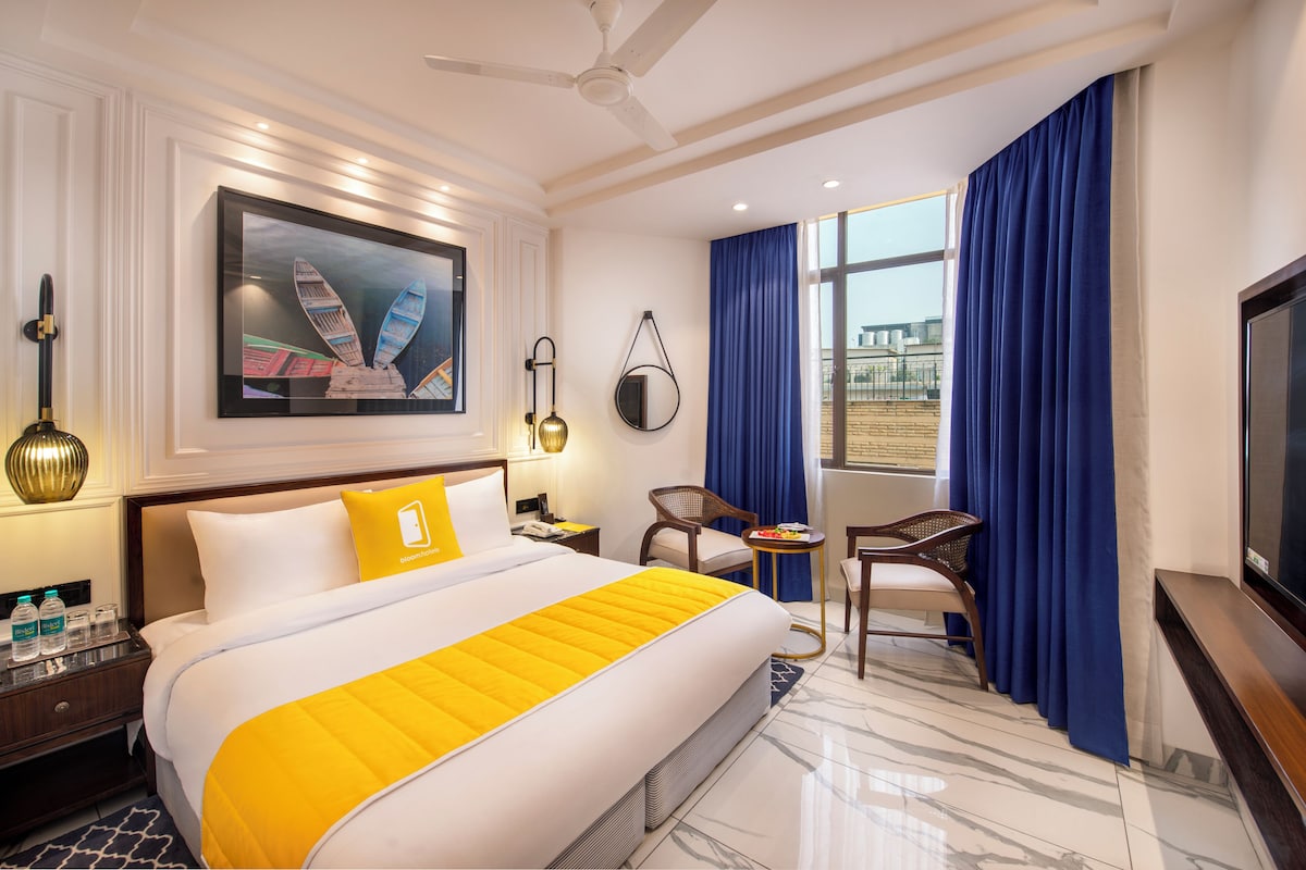 A hotel room with a large bed, a desk, a chair, a TV, and a window with curtains.