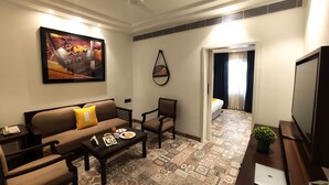 A hotel room with a sofa, armchairs, a coffee table with breakfast, a TV, and a painting on the wall. - Bloom Boutique Gk-1 (New Delhi)